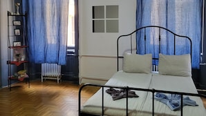 A bedroom with a metal bed frame, a radiator, a wooden floor, and a shelf with books and a plant. - Casa Nora Guest House (Budapest)