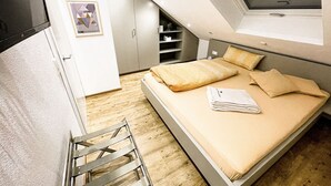 Un dormitorio compacto con cama elevadas, un pequeño rincón de descanso y una ventana con vistas.
