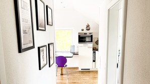 Un pasillo que conduce a una cocina con piso de madera, paredes blancas y cuadros en la pared izquierda.