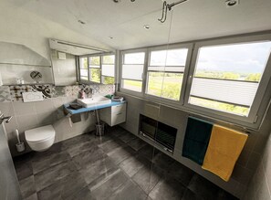 Un baño moderno con inodoro, lavamanos, espejo y ventanas amplias con vistas al exterior.