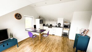 Una cocina moderna con armarios blancos, horno integrado y microondas. Hay una zona de comedor con una mesa y sillas moradas.