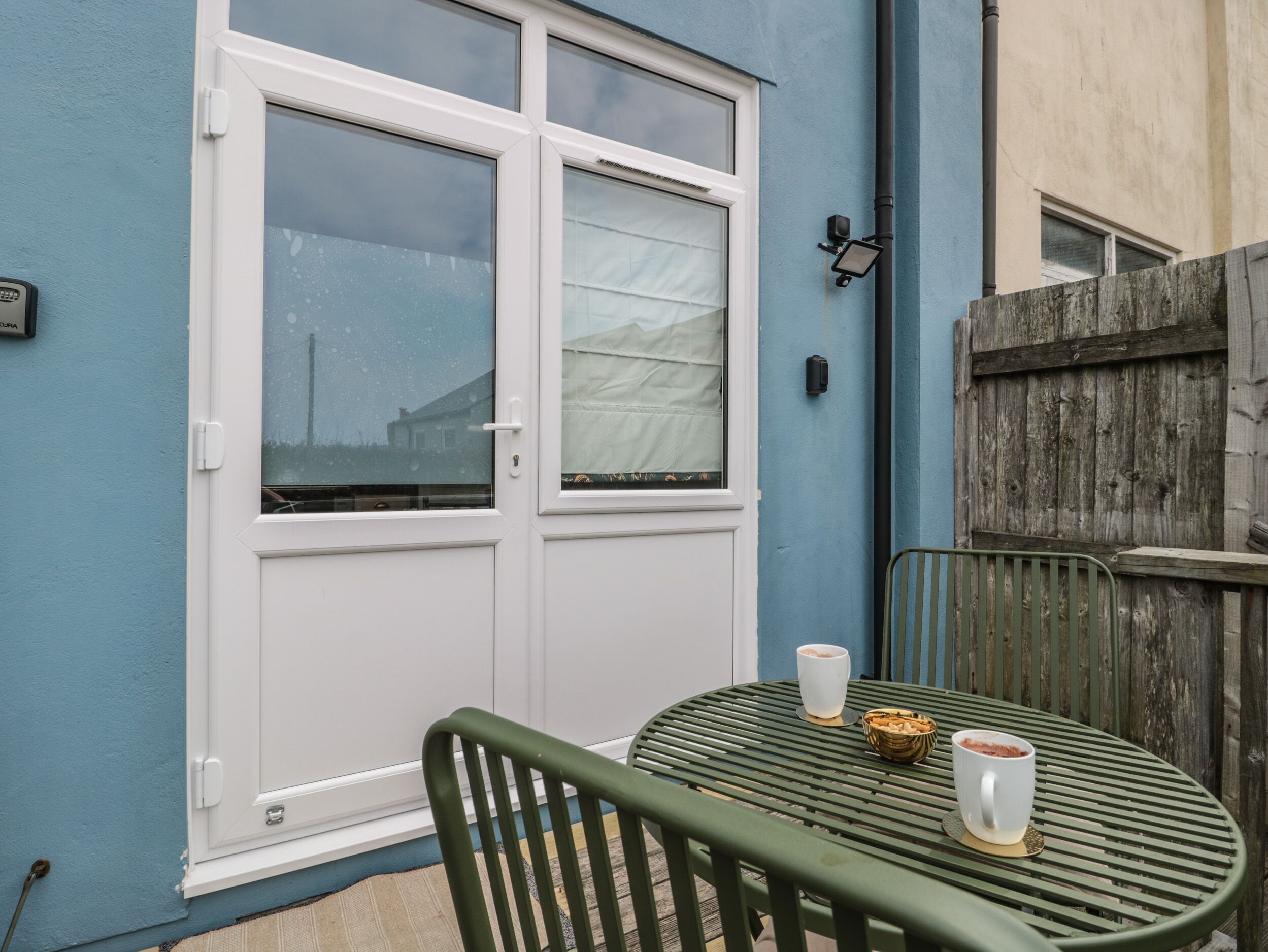 Un patio con mesa y sillas, una ventana con cortinas y una valla de madera.