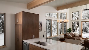 A modern kitchen with a large island, wooden cabinets, and a view of a snowy landscape through large windows. - Owl Ridge Cabins (Wausau)