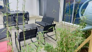En terrasse med et bord og stole, omgivet af høje planter.