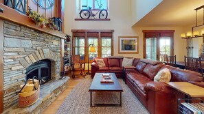 A spacious living room with a stone fireplace, leather sofa, and a dining area with wooden chairs.