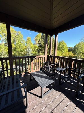 A covered outdoor deck with wooden railings, a table, and two chairs.