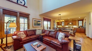A spacious living room with a large sectional sofa, a coffee table, and a dining area with wooden furniture.