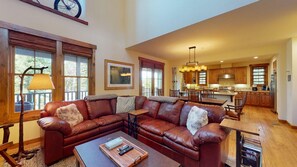 A spacious living room with a large sectional sofa, a coffee table, and a dining area with wooden furniture.