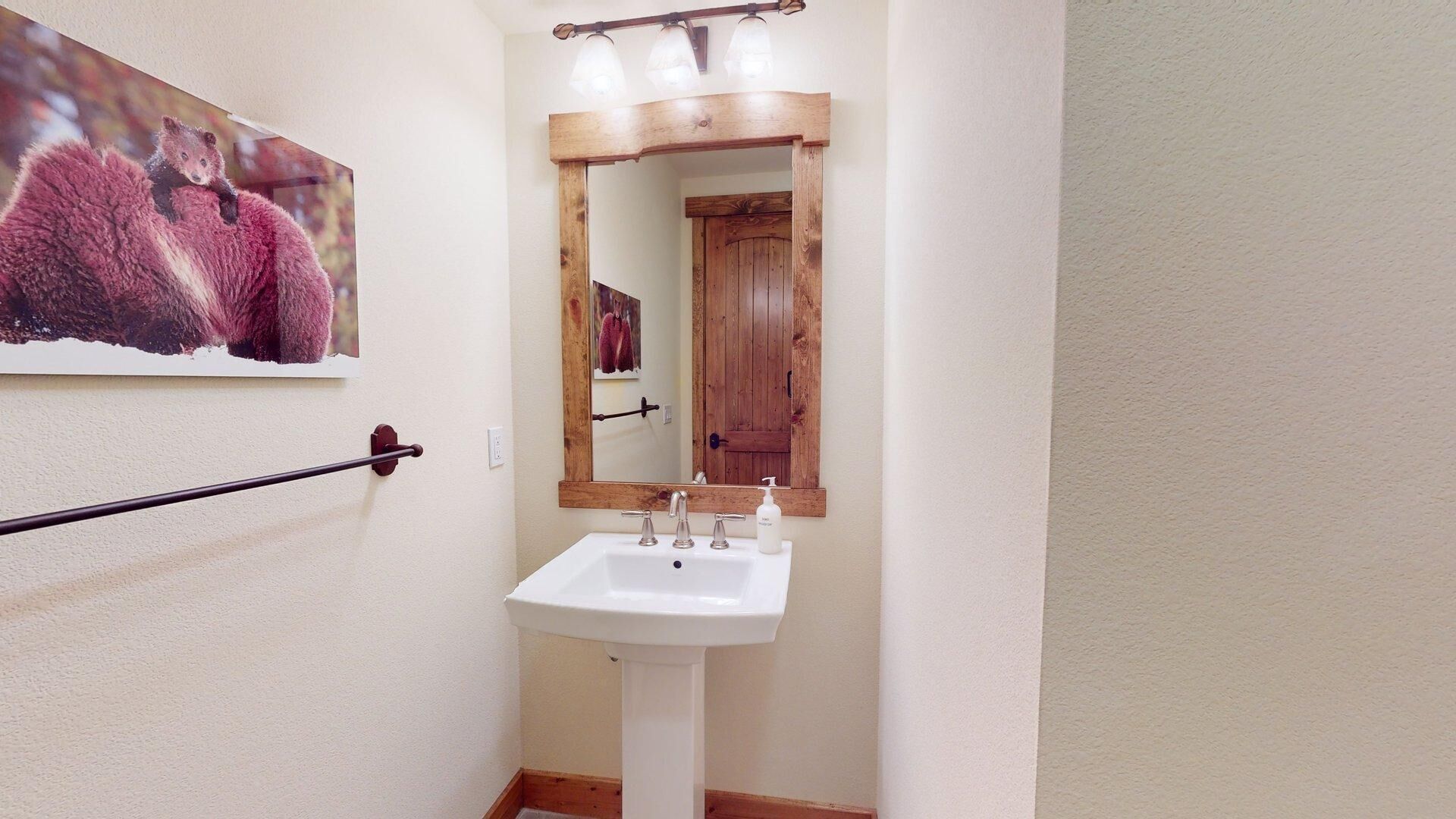Un baño con un lavamanos blanco, una puerta de madera y un espejo con marco de madera.