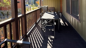 A covered outdoor area with a wooden deck, metal railing, and a table with chairs.