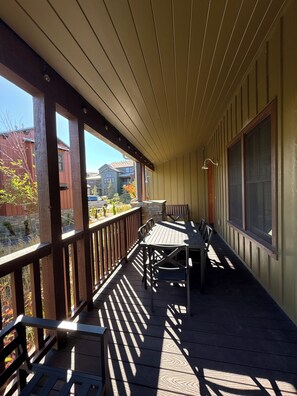 A covered outdoor area with a wooden deck, metal railing, and a table with chairs.