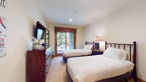 A bedroom with two beds, a TV, a dresser, and a window with a view of trees. - Snowcreek Resort Vacation Rental 1501 (Mammoth Lakes)