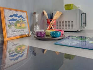 A kitchen counter with a framed picture, a set of wooden utensils, a red utensil holder, and a microwave. - Gîtes Arc-en-ciel (Saint-François)