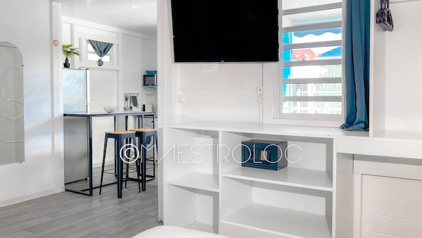 A modern hotel room with a bed, a TV, a desk, and a view of the outside. - Gîtes Arc-en-ciel (Saint-François)