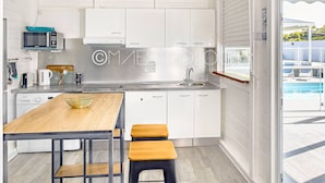 A modern kitchen with white cabinetry, a stainless steel sink, and a wooden dining table with two stools. - Gîtes Arc-en-ciel (Saint-François)