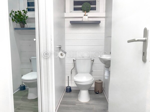 Un baño pequeño con dos inodoros, un lavamanos y un cubo de basura.