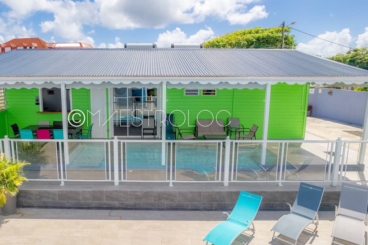Een groen gebouw met een zwembad, terras en een overdekte patio.