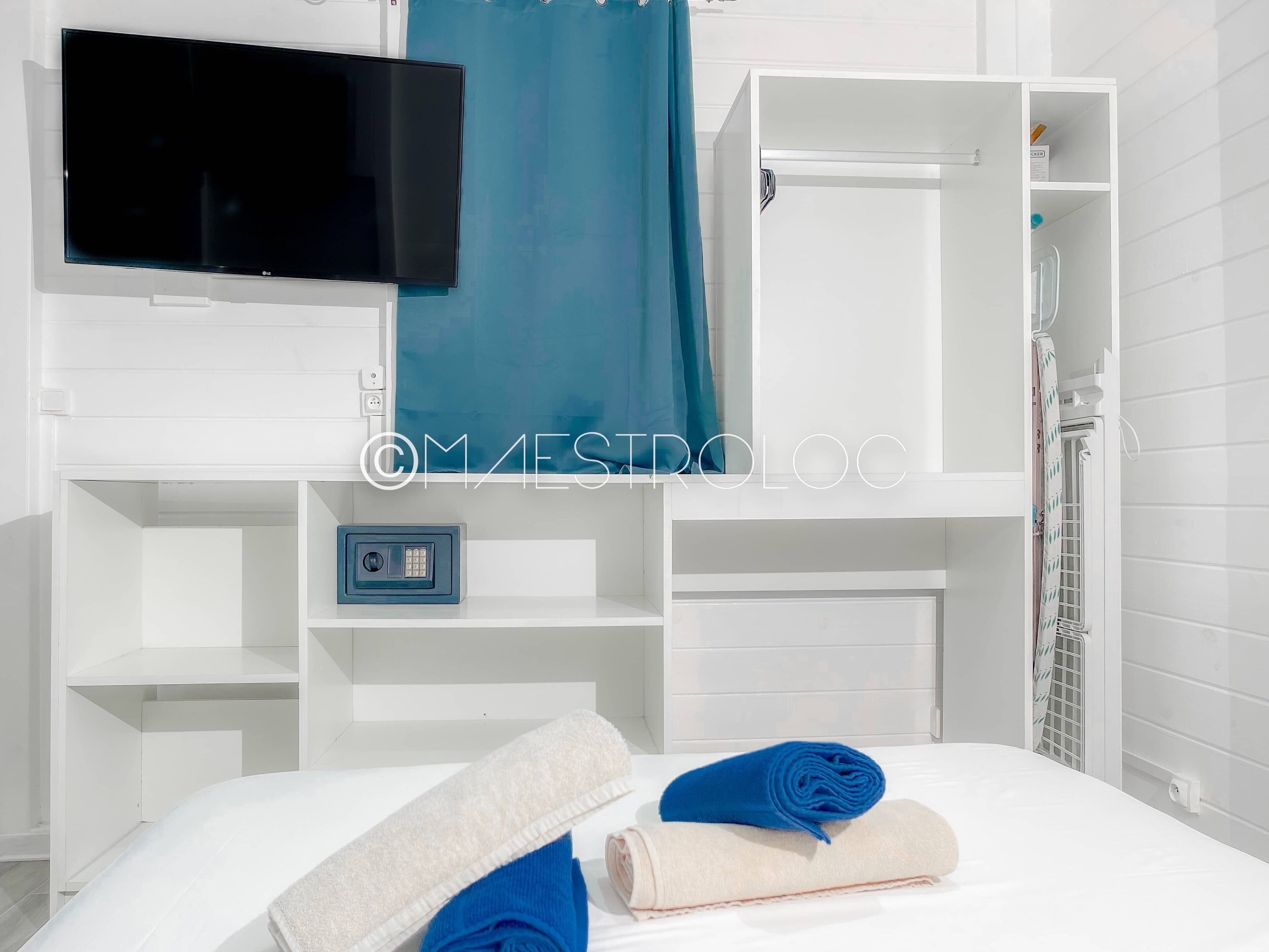 A modern hotel room with a flat-screen TV, a shower area, and neatly folded towels.