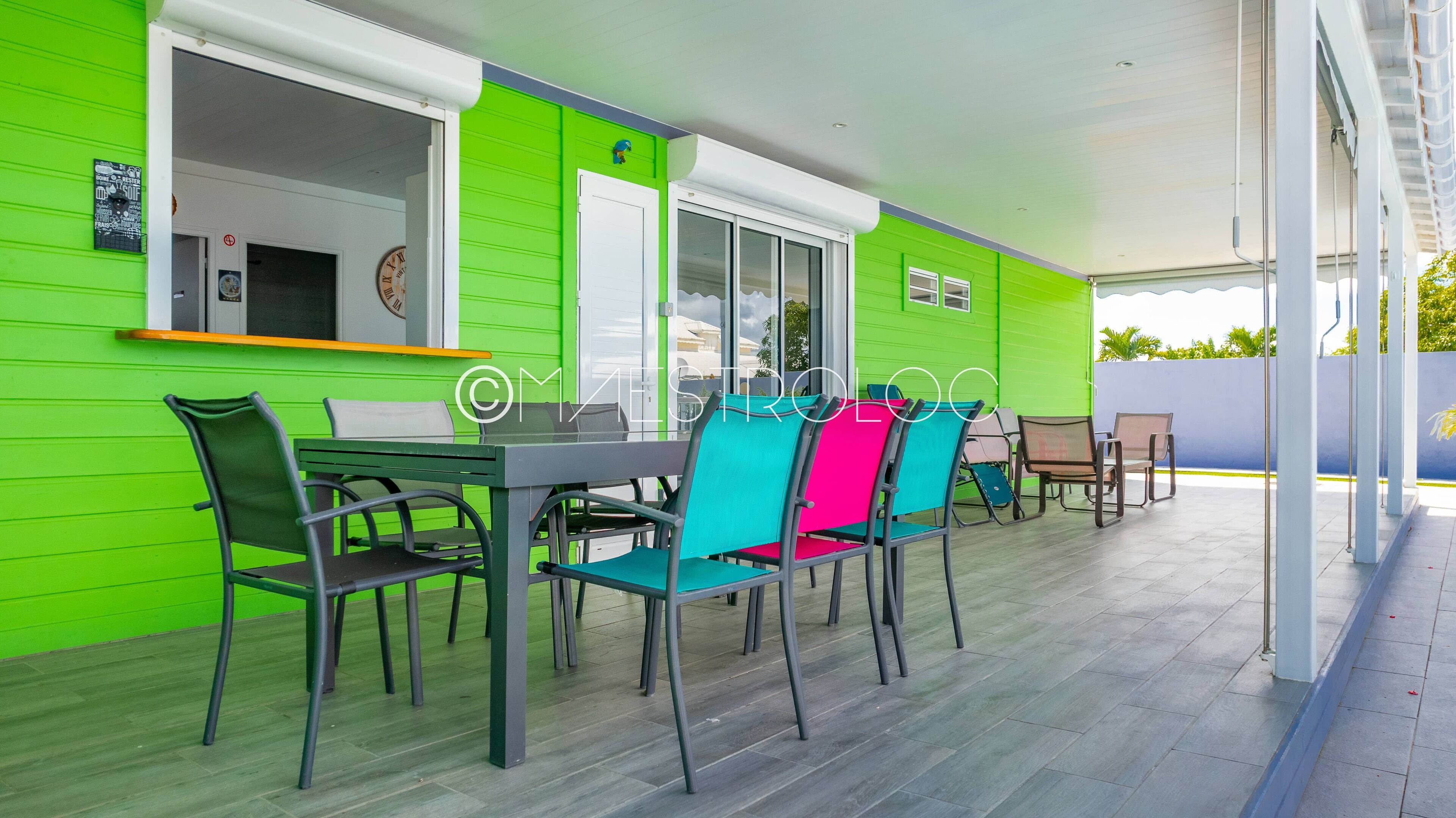 A covered patio area with a table and chairs, a window with a view, and a green wall.