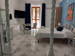 Una camera d'albergo con un letto, una scrivania, una sedia, una TV e una finestra con tende.