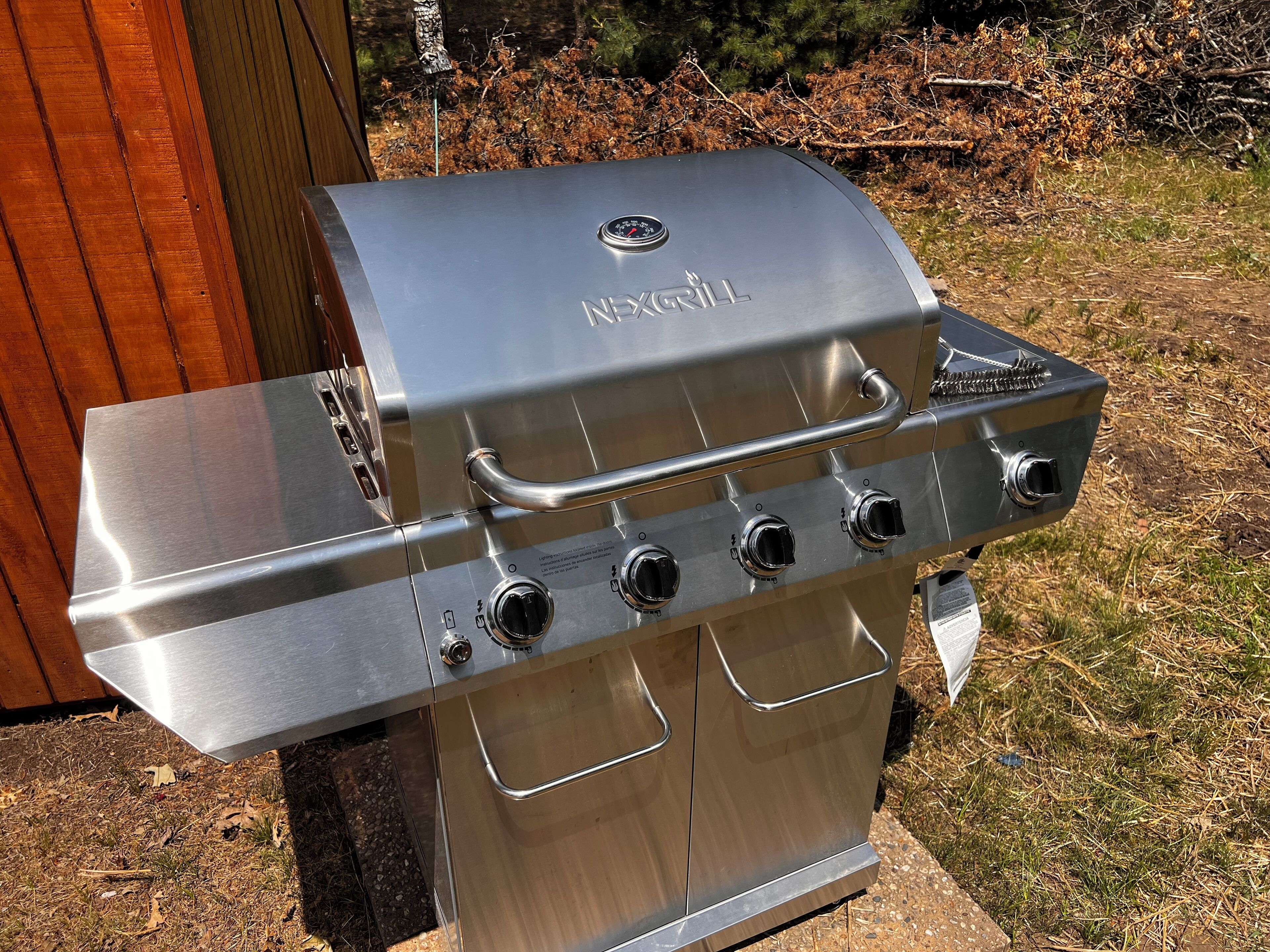 A stainless steel outdoor grill with four burners, a side shelf, and a control panel.