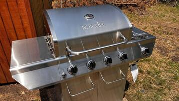 A stainless steel outdoor grill with four burners, a side shelf, and a control panel.