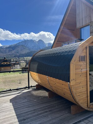 A wooden cabin with a curved roof, a balcony, and a view of snow-capped mountains.