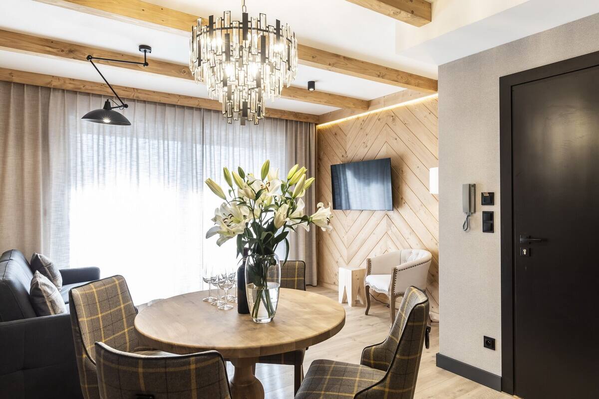 Un comedor moderno con una mesa redonda de madera, sillas a cuadros, un jarrón de flores y una araña.