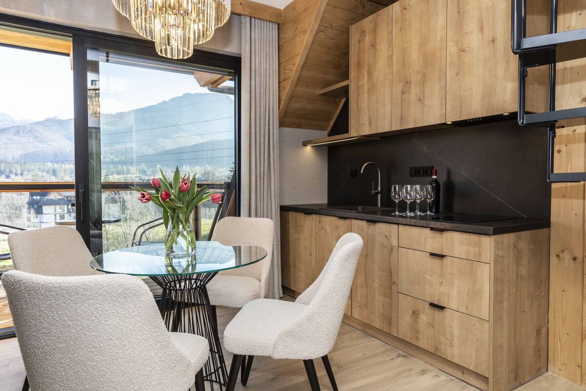 Una cocina moderna con armarios de madera, encimera negra y una mesa de comedor de vidrio con sillas blancas.