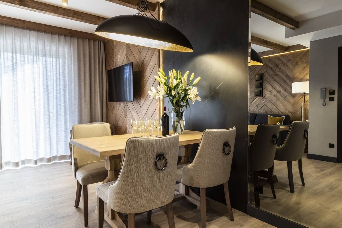Un moderno comedor con una mesa de madera, seis sillas, un jarrón de flores y una lámpara colgante grande.