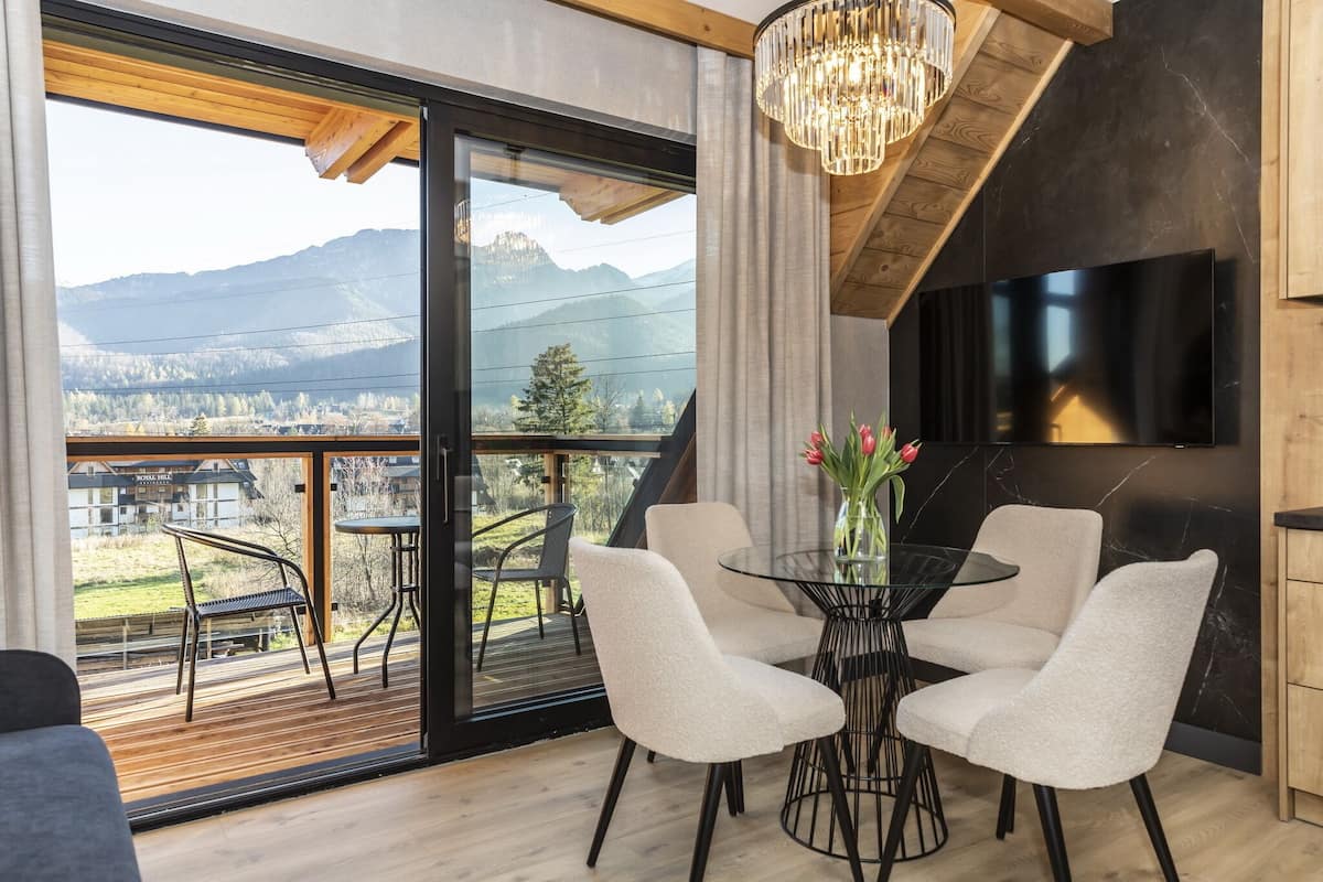 Una habitación moderna con un ventanal grande, una mesa de comedor con sillas, una araña y un televisor de pantalla plana montado en la pared.