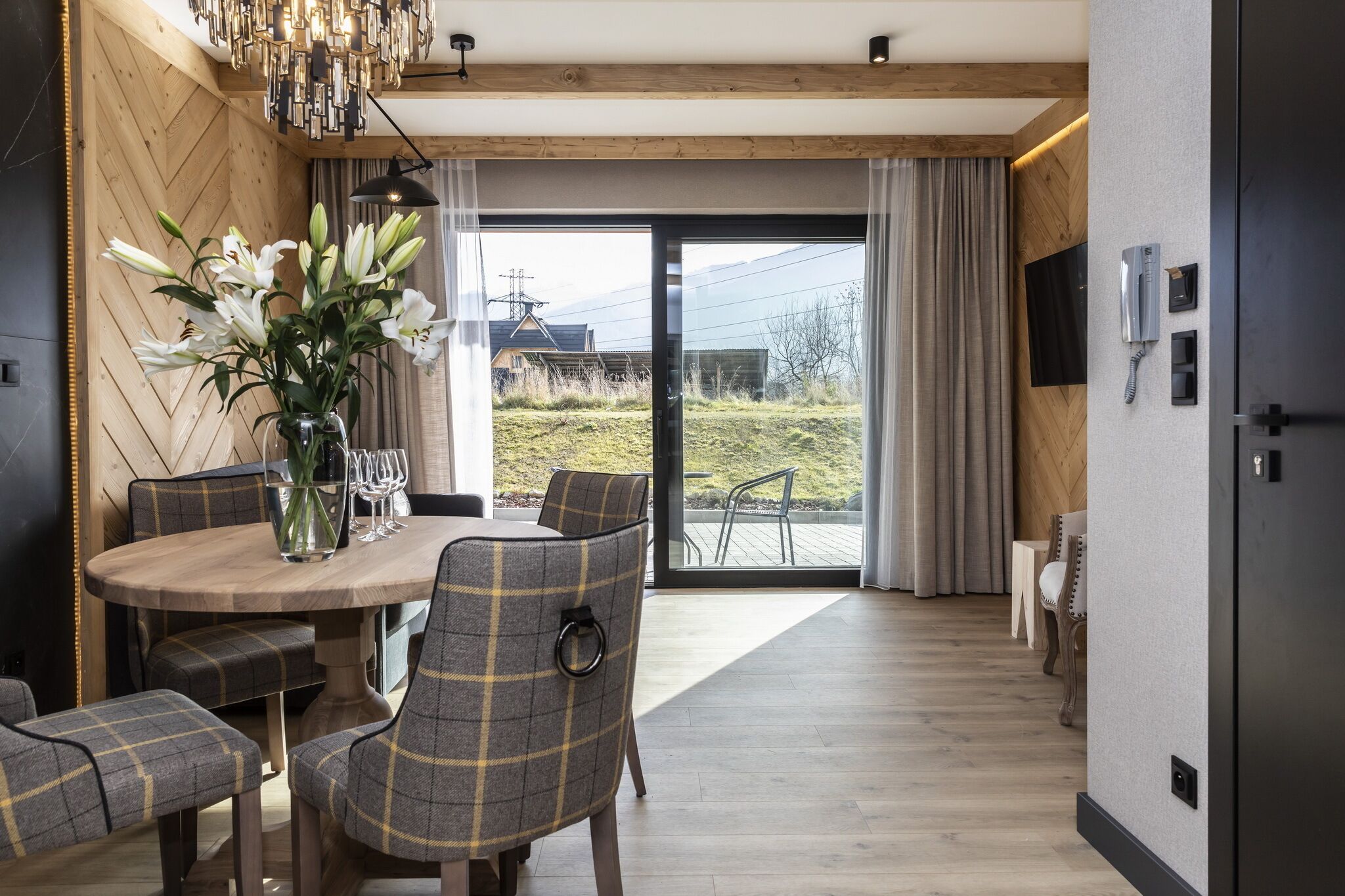 A modern dining area with a wooden table, plaid chairs, and a vase of flowers.