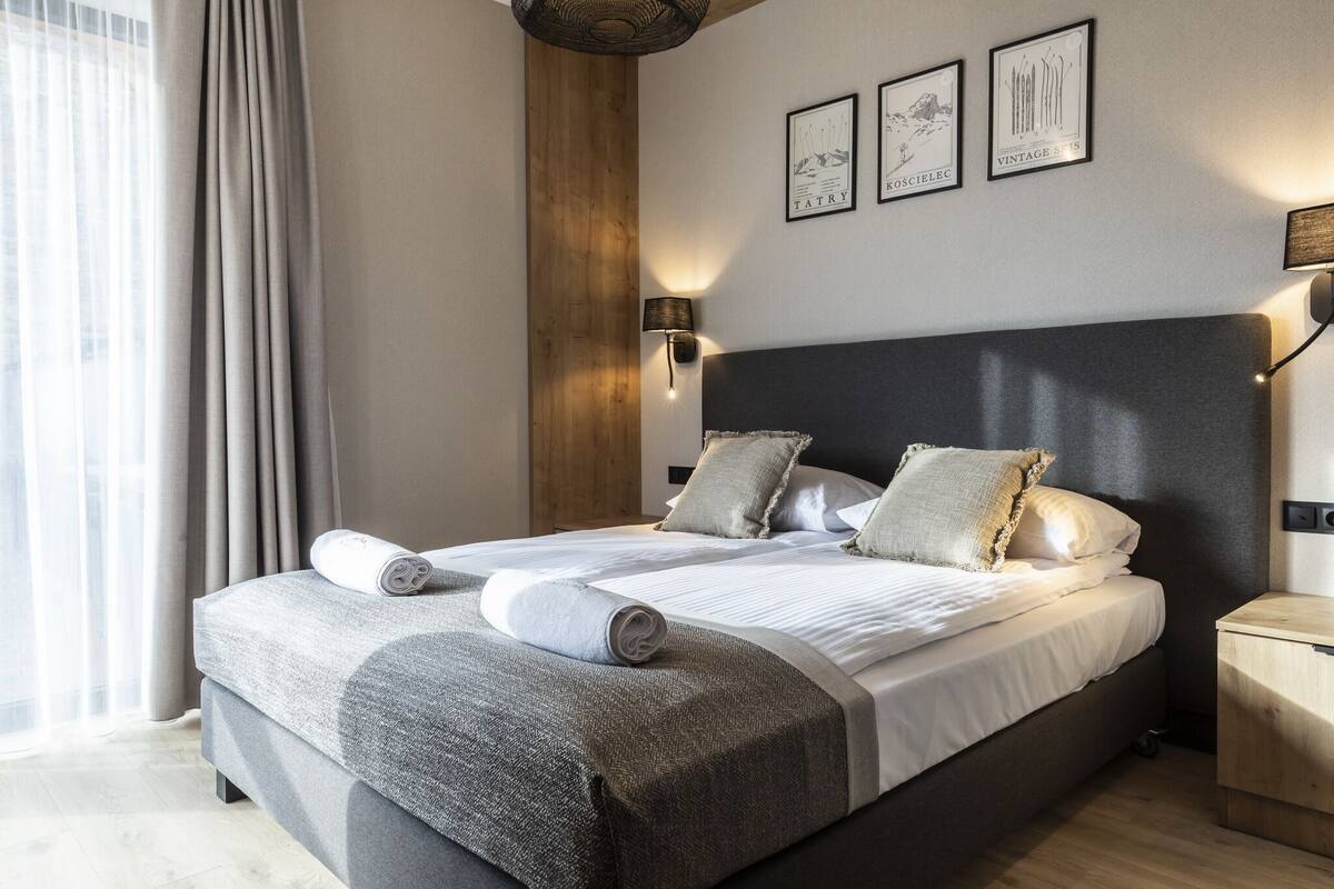 Un dormitorio moderno con una cama grande, dos lámparas fijadas a la pared y tres cuadros enmarcados.