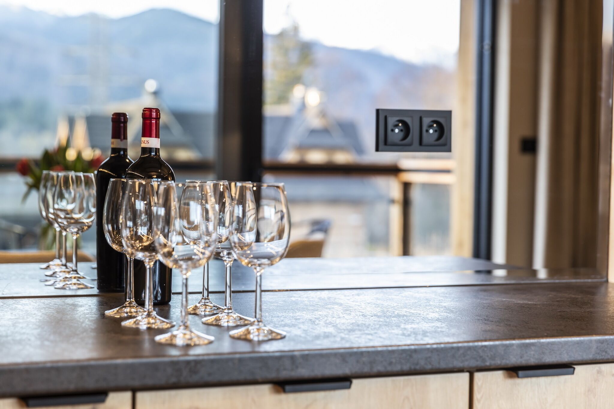 Zona de bar con botellas de vino y copas sobre una barra, con vistas a un paisaje pintoresco.