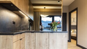 A modern kitchen with wooden cabinets, a black countertop, and a view of mountains through a large window.