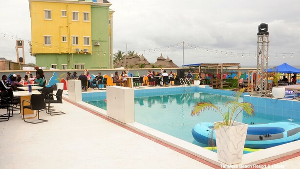 A pool area with a dining setup and a large building in the background. - Timeless Beach Resort and Hotels (Lekki)
