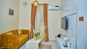 A living room with a sofa, a coffee table, a TV, and a wall-mounted air conditioner. - Timeless Beach Resort and Hotels (Lekki)