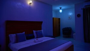 A dimly lit hotel room with a large bed, a wardrobe, a chair, and a ceiling fan. - Timeless Beach Resort and Hotels (Lekki)