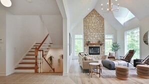 A spacious living room with a fireplace, a staircase, and a large window. - 11,000sqft sleeps 29, w/ POOL! private lake, hiking trails, hot tub, 130 acres! (Logan)