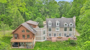 A large, two-story log cabin with a deck and a separate building with a balcony. - 11,000sqft sleeps 29, w/ POOL! private lake, hiking trails, hot tub, 130 acres! (Logan)