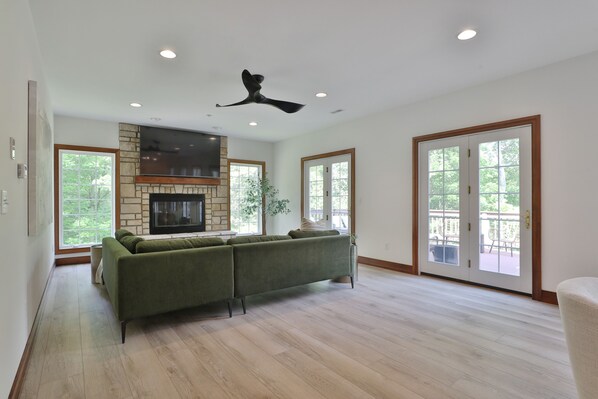A spacious living room with a sectional sofa, a stone fireplace, and a ceiling fan.