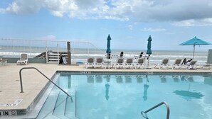 A pool area with lounge chairs and umbrellas, a clear view of the ocean, and a fenced deck. - Ocean View Studio • Steps to Beach (Daytona Beach)