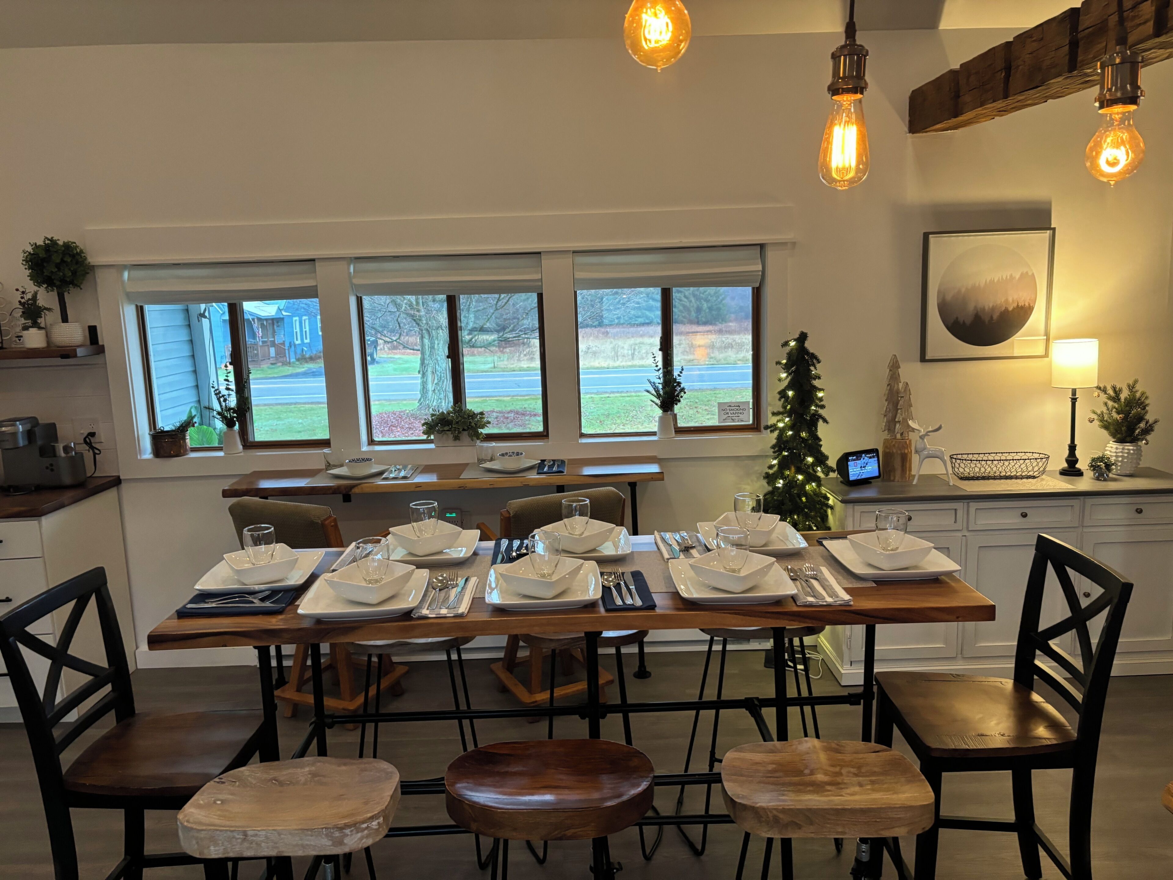 A dining area with a long table set for multiple people, chairs, and a small Christmas tree.