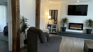 Ein modernes Wohnzimmer mit einem grauen Sofa, einem Kamin und einem an der Wand befestigten Flachbildfernseher.