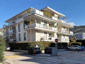 A multi-story residential building with balconies, a no-entry sign, and a parking area with cars.