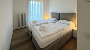 A modern hotel room with two beds, a radiator, and a window with sheer curtains. - Apartment with a beautiful terrace (Riva del Garda)