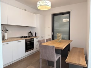 Een moderne keuken met witte kasten, een houten aanrechtblad en een inbouwoven. Er staat een eettafel met stoelen en een decoratieve vaas.