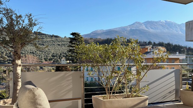 A balcony with a view of a mountain, a potted plant, and outdoor furniture. - Apartment with a beautiful terrace (Riva del Garda)
