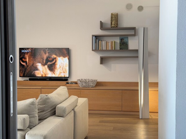 A modern living room with a flat-screen TV, a sofa, wooden flooring, and built-in shelves with books and decorative items.