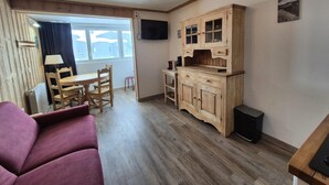 A cozy living room with a sofa, wooden dining table, chairs, a kitchen area with cabinets, and a television. - 100m from resort center, Ground floor, tv, ski locker, 29m², Tignes (Tignes)